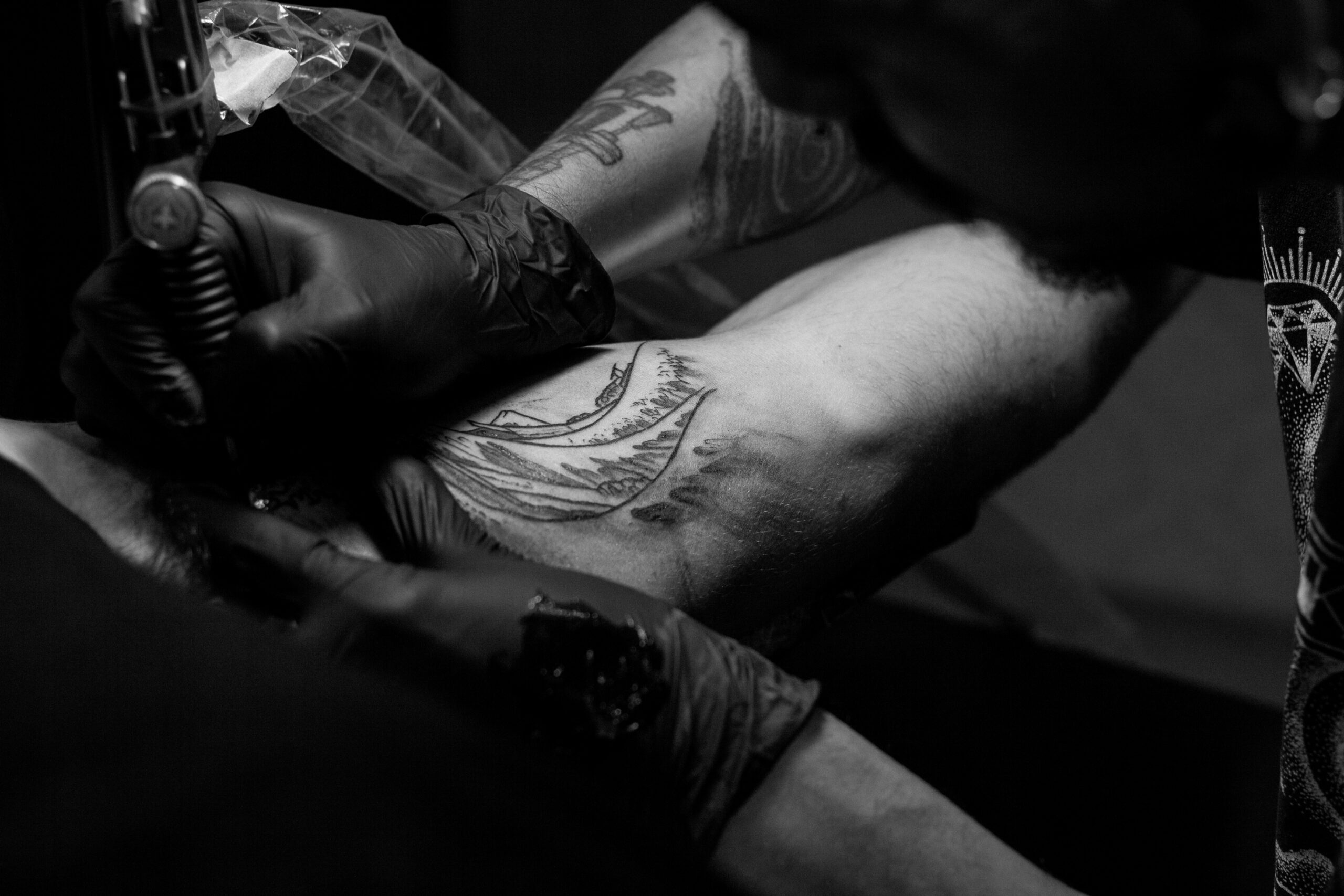 grayscale photo of man doing tattoo