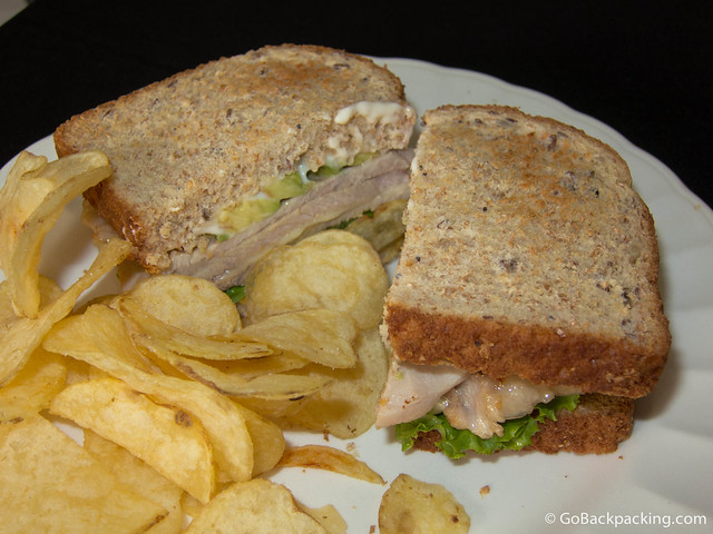 Ham and cheese sandwich with avocado, and a side of potato chips